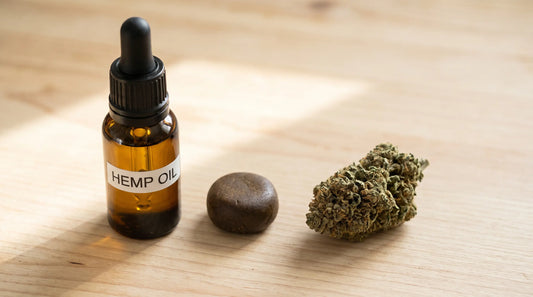 Flacon d'huile, morceau de résine et fleur de CBD disposés côte à côte sur une table en bois