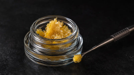 Gros plan sur un petit contenant de concentré de CBD avec un outil de dab posé à côté